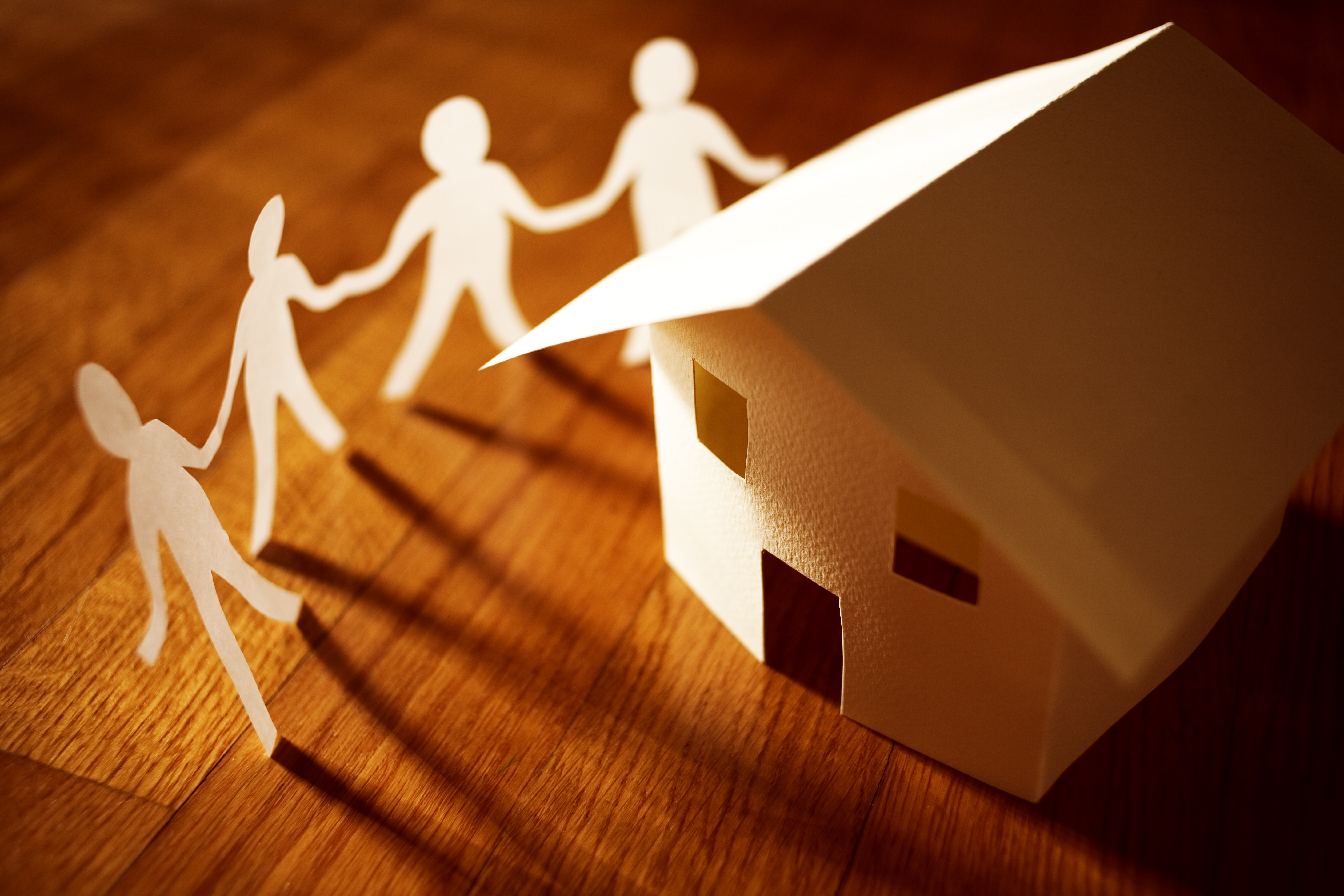 Paper cut-outs of stick people holding hands around a paper build house
